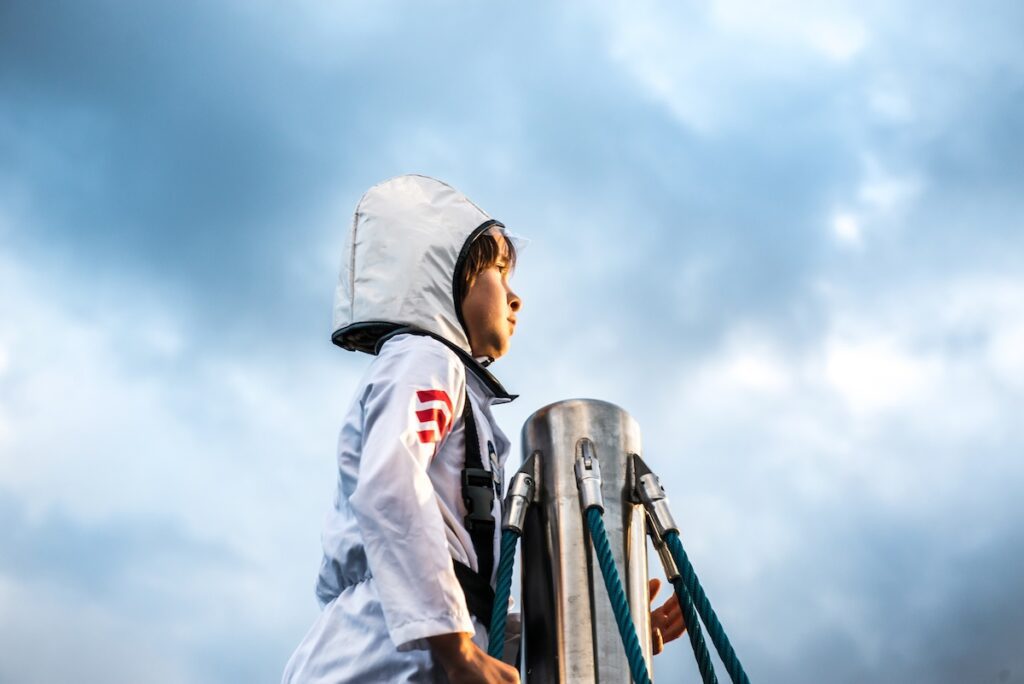 child in an astronaut looking out to the horizon from near the top of a pole.