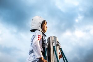 child in an astronaut looking out to the horizon from near the top of a pole.